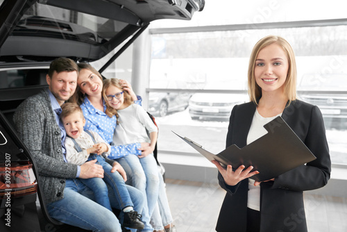 Female car dealer looking at camera and posing in auto salon