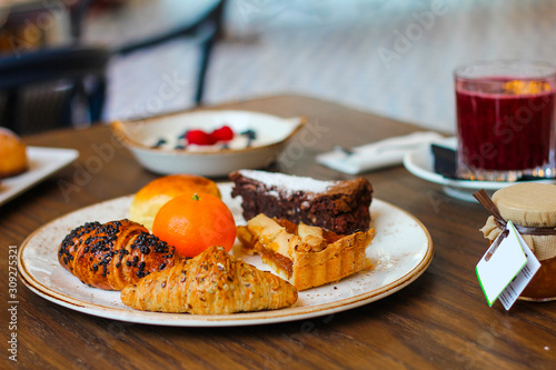 detail of breakfast table with chocolate cakes, jam, red orange juice, mandarin, croissants, butter, yogurt with raspberries and blueberries