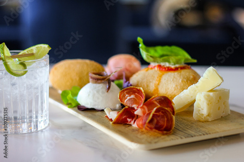 gin tonic with lemon and a tray of typical Napolitan snacks such as buffalo mozzarella, savory puff pastry, black pig salami from Caserta, ham and cheese