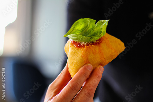hand holding a montanara, tipical street food fried with tomato, mozzarella, basil and parmesan cheese from naples, italy photo