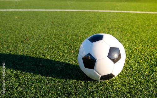A soccer ball lying on the football pitch. Green grass  white line  hard shadow.