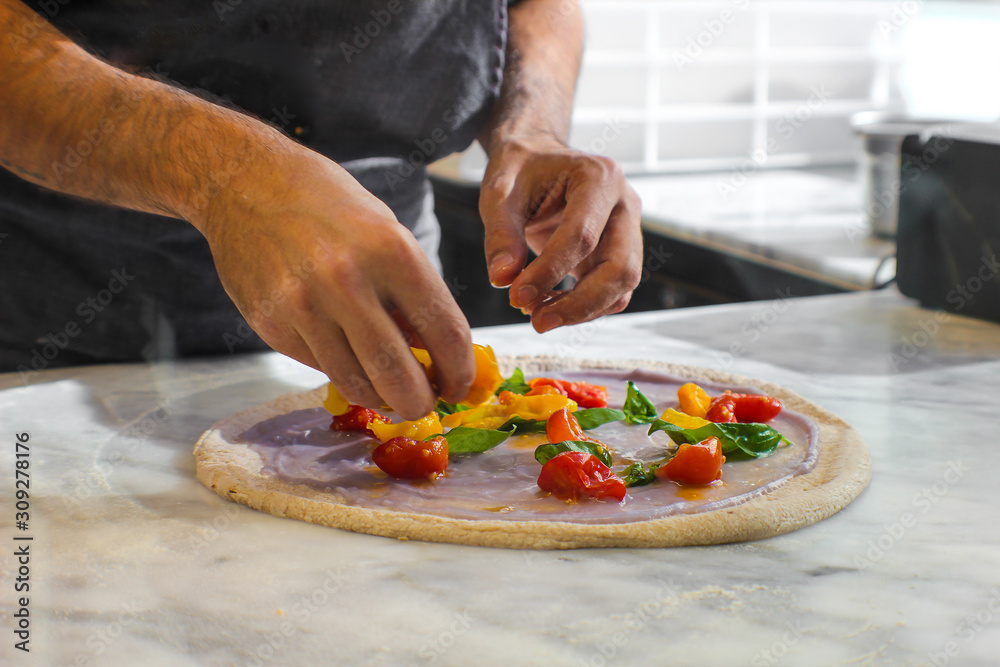 preparation of Pizza Bio in a traditional Italian pizzeria, prepared with wholemeal dough left to rest for at least 48 hours. On a base of purple potato velvety, there are red and yellow Piennolo cher