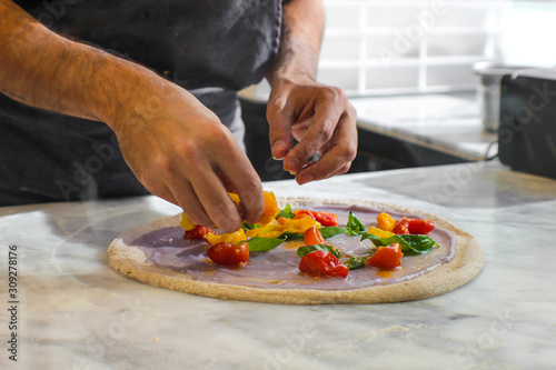 Fototapeta Naklejka Na Ścianę i Meble -  preparation of Pizza Bio in a traditional Italian pizzeria, prepared with wholemeal dough left to rest for at least 48 hours. On a base of purple potato velvety, there are red and yellow Piennolo cher