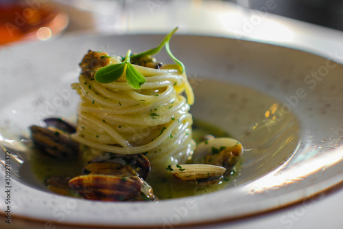 plate of spaghetti with clams and extra virgin olive oil in a stew of fish, parsley and a glass of wine. Fine serving in a luxury Italian restaurant