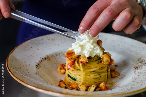 chef's hands plating a dish with spaghetti with lobster and buffalo stracciatella. In a luxurious Italian restaurant