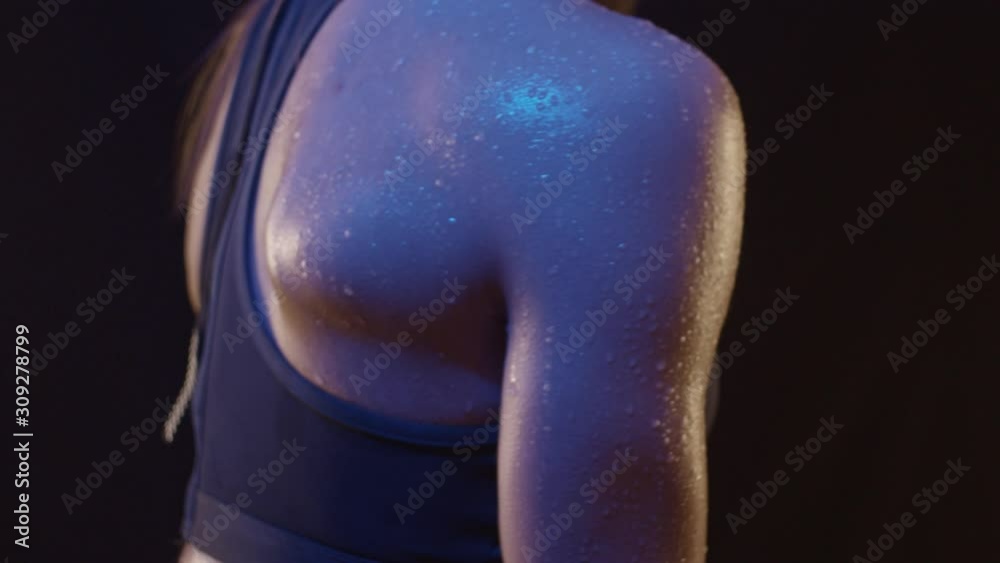 Arm muscles of fit woman under colored light with drops of water, close up, shot in slow motion Arm muscles of fit woman under colored light with drops of water, close up, shot in slow motion