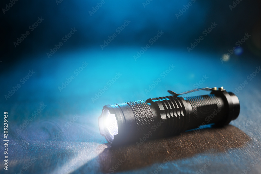 Tactical waterproof flashlight. LED flashlight shines on the table in smoke. Tactical waterproof flashlight. LED flashlight shines on the table in smoke.