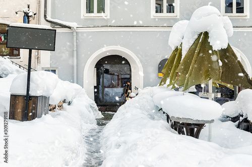 European city street snowcapped after blizzard snowfall. Outdoor cafe tables and umbrellas covered with heavy snow layer. Emty urban cityscape with bad christmas weather photo