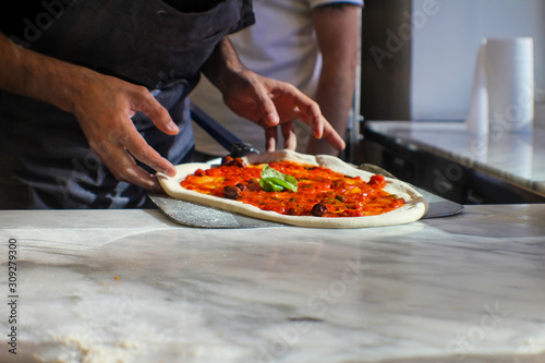 pizza maker is preparing a Gourmet pizza with San Marzano tomato sauce, black olives, capers, fresh basil, EVO oil and a sprinkling of pecorino in an Italian pizzeria