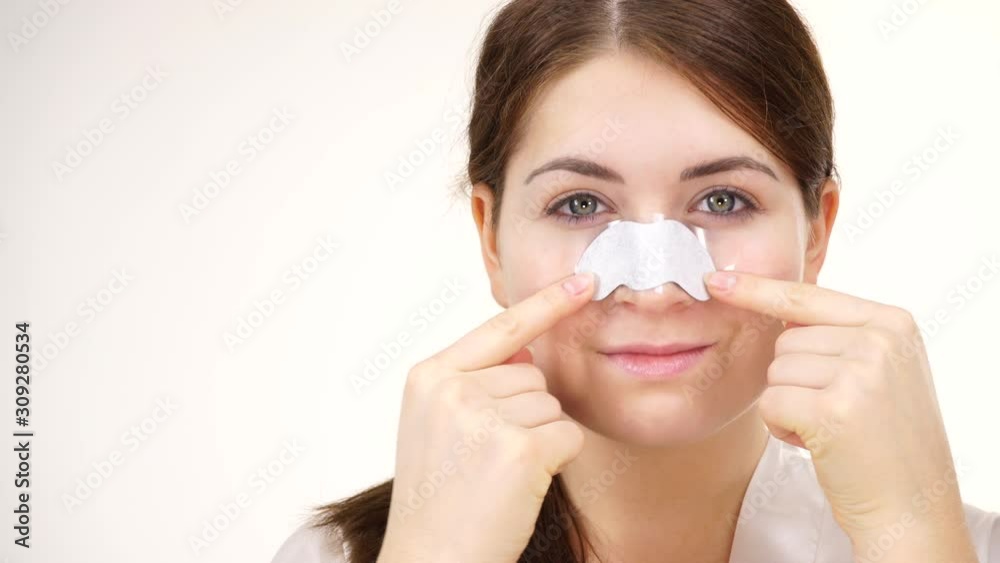 Woman appying clear-up strips on nose, using pore cleansing textile mask, against white. Girl taking care of skin complexion. Beauty treatment. Skincare Woman appying clear-up strips on nose, using pore cleansing textile mask, against white. Girl taking care of skin complexion. Beauty treatment. Skincare
