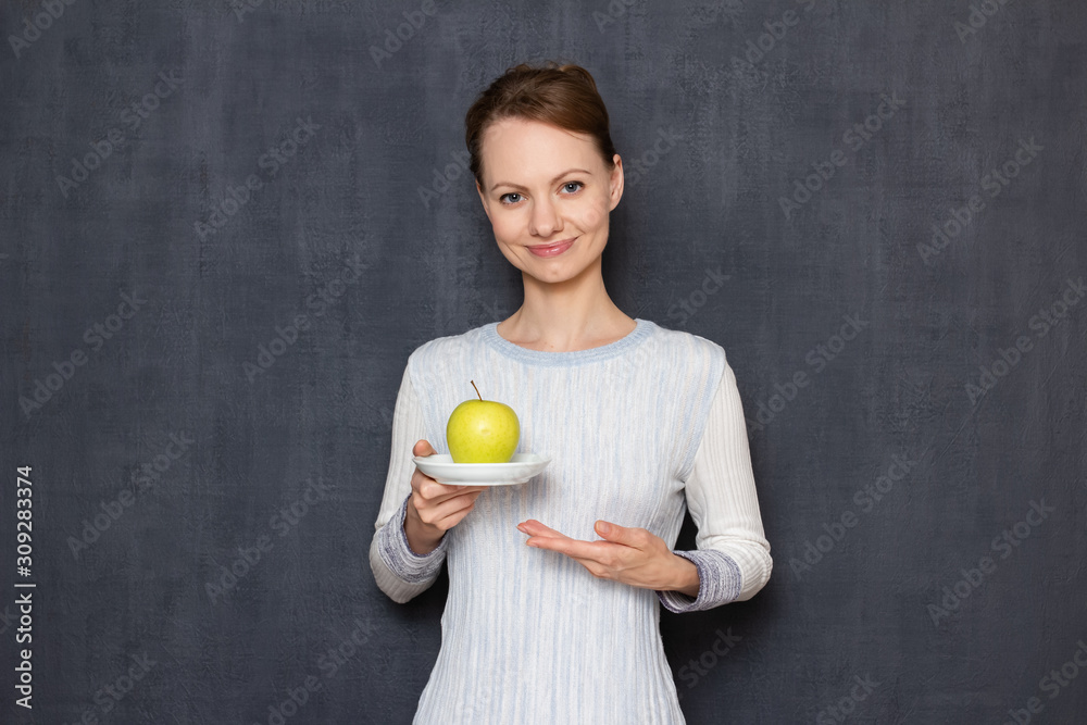 Portrait of happy girl smiling and pointing at plate with yellow apple