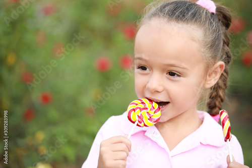 Cute little girl with sweet lollipop outdoors