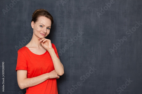 Portrait of happy focused young woman touching chin with one hand