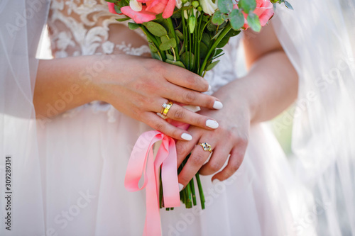 The bride holding a lush bridal bouquet of roses and a lot of greenery. Stylish wedding bouquet on the sunset background