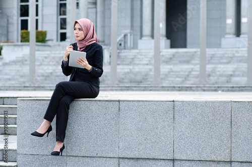 Portrait of cheerful happy businesswoman wearing black suit  sitting and holding tablet © amirul syaidi