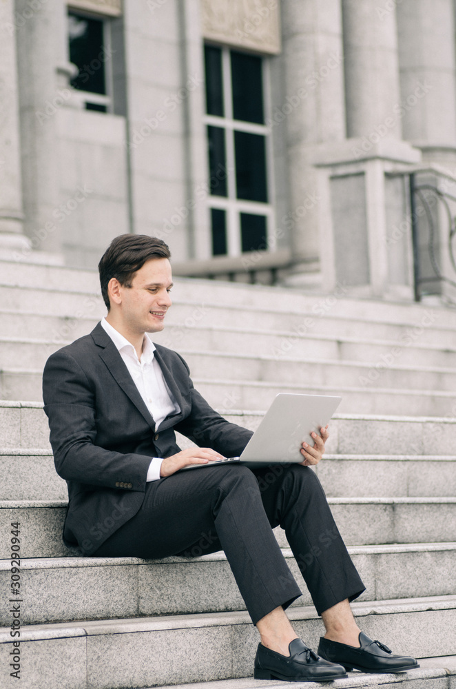 smiling young business man sitting on stairs and working with his laptop smiling young business man sitting on stairs and working with his laptop