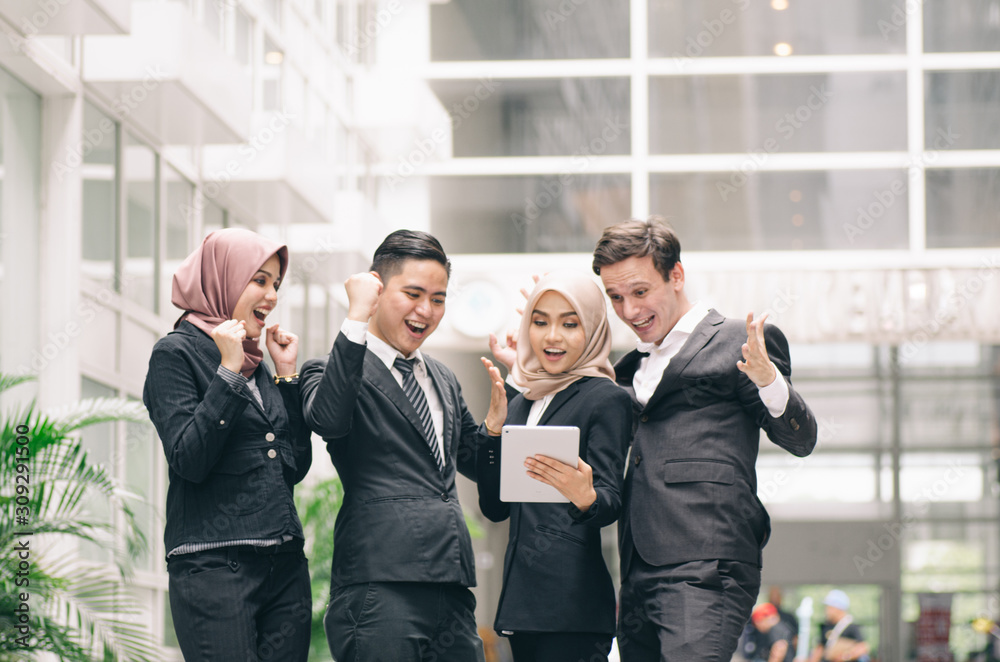 Happy successful young business people look at tablet and cheer their success Happy successful young business people look at tablet and cheer their success