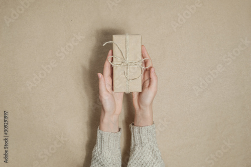Slika na platnu Human hands gives away a gift in brown paper on matching background