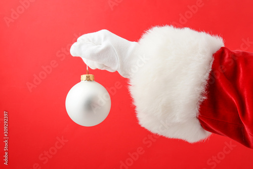 Hand of Santa with Christmas ball on color background