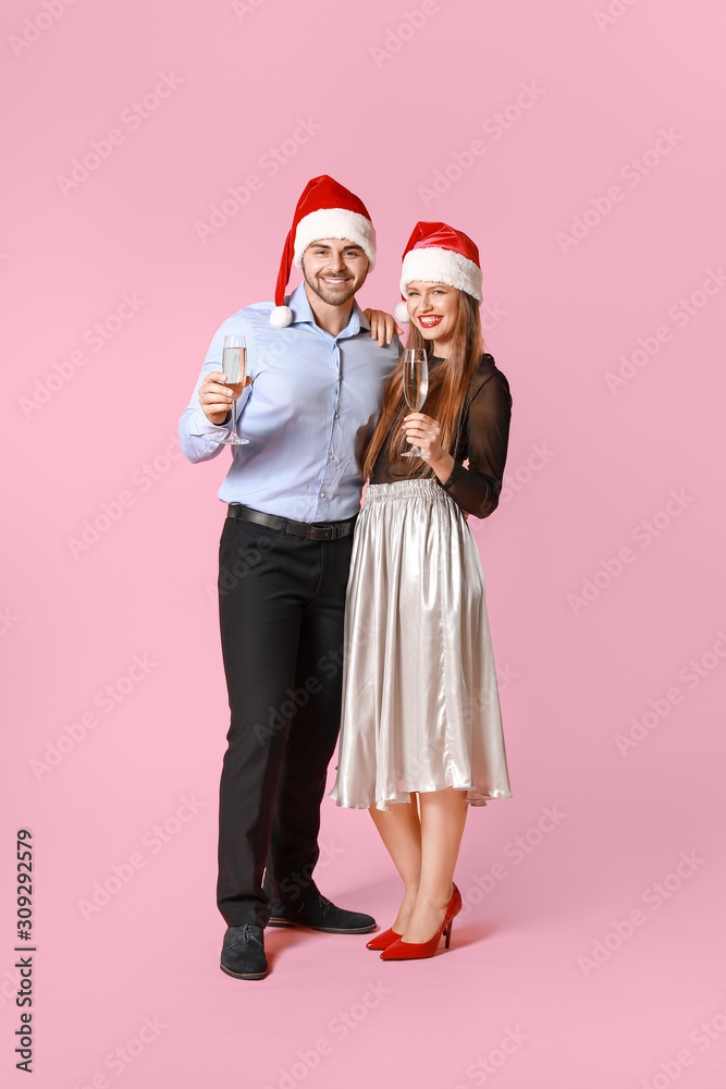 Obraz premium Happy couple in Santa Claus hats and with glasses of champagne on color background