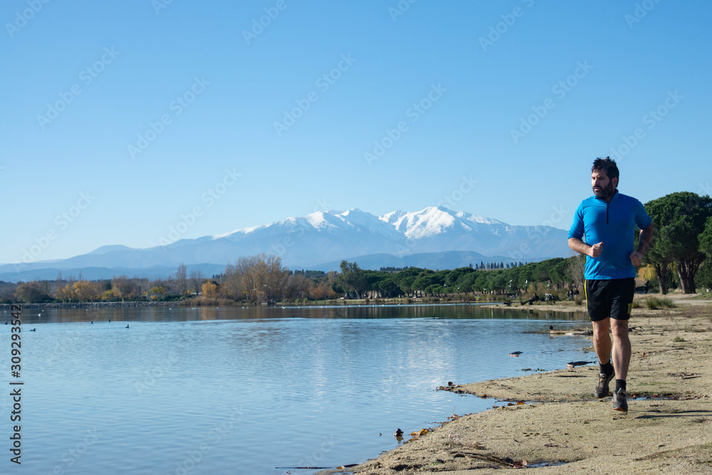 Man running on a lake. Running through nature.Lake of Villeneuve de la Raho (France) overlooking the Pyrenees and the Canigo