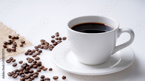 Cup of black coffee and coffee beans and jute on white 