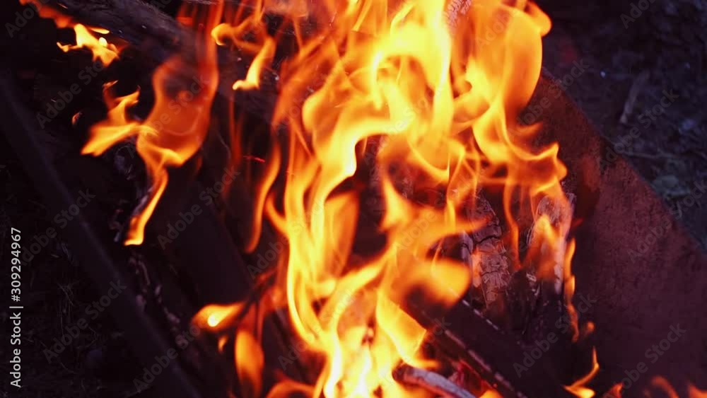 In the evening firewood burns in a charcoal grill.