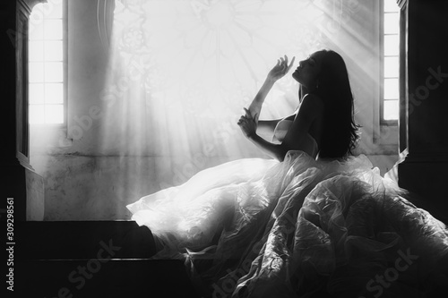 black and white silhouette portrait of bride in white dress sitting on stairs infrontof window with sunlight pass through photo