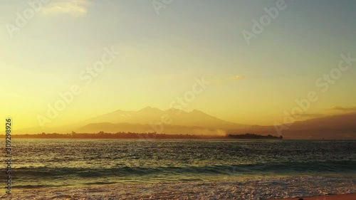 foamy waves splashing on the sandy beach. tropical island in the background. golden hour and romantic sunset photo