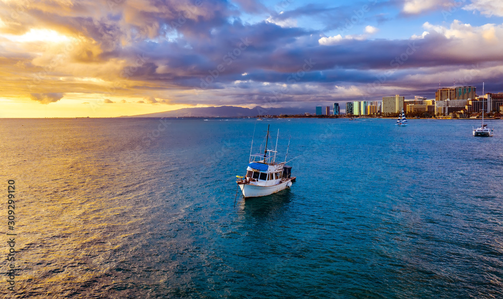 Fishing boat at sunset in Hawaii paradise with perfect clouds and orange and blue reflections in ocean