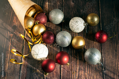Christmas gifts, gold, silver, red Christmas balls spilled out from a package of kraft paper on a wooden background. Christmas balls. Copyspace.