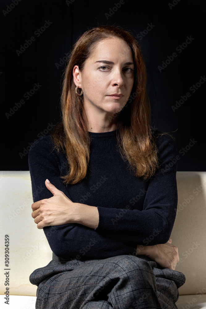 Portrait of a mature woman 45 - 50 years, serious, pensive, looking camera with crossed arms over black background. Portrait of a mature woman 45 - 50 years, serious, pensive, looking camera with crossed arms over black background.