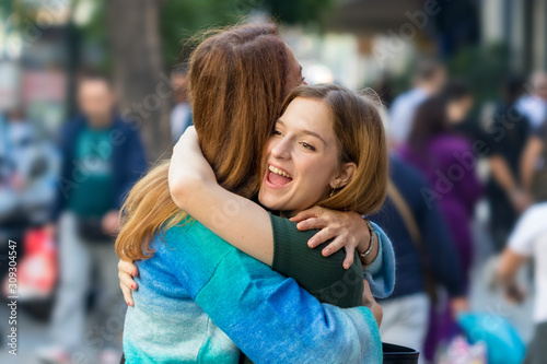 Happy teenage girl hugging her mother on the street, outdoors. © Ruben