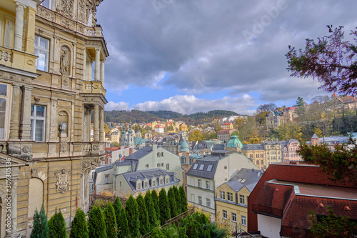 Scenic aerial view of Karlovy Vary - small ancient touristic resort town near the border between Czech Republic and Germany. Beautiful summer cloudy look of little famous town among hills in Czechia