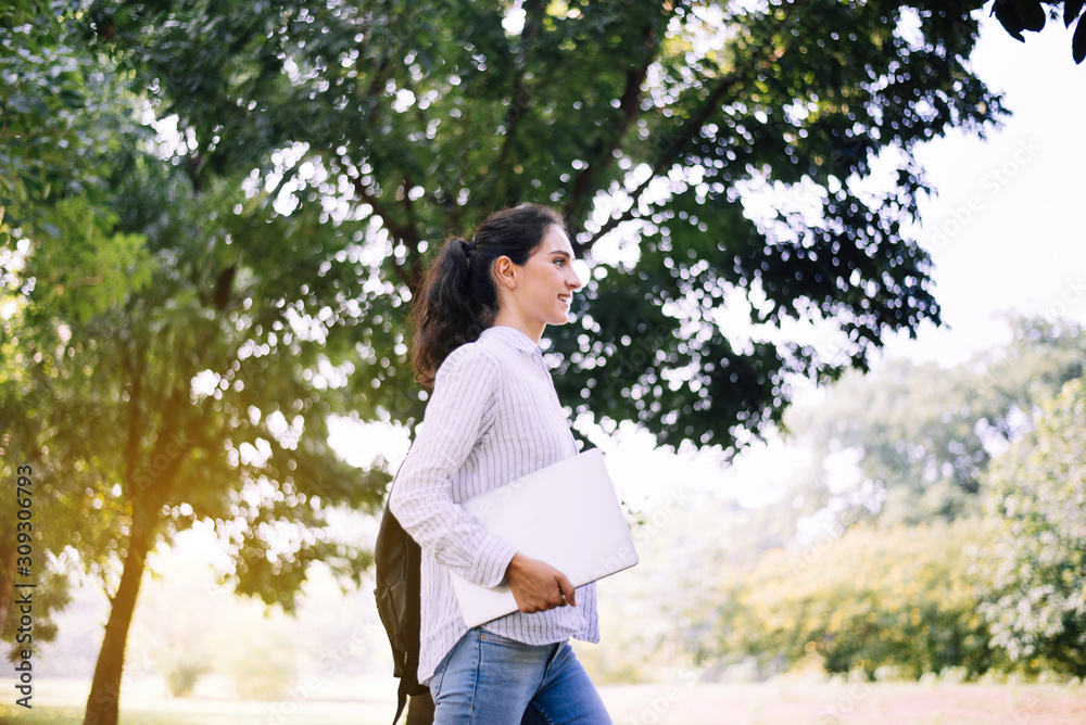 Beautiful young woman holding laptop computer and walking at public park in the morning,Happy and smiling Beautiful young woman holding laptop computer and walking at public park in the morning,Happy and smiling
