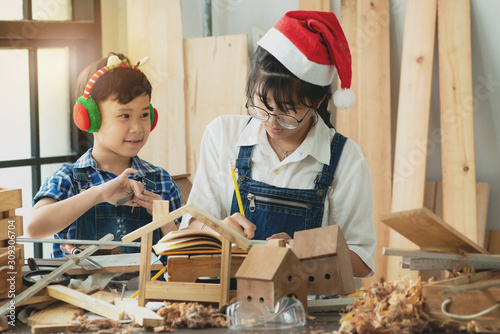 Asian brothers and sisters with woodwork in carpentry workshop, with Christmas earmuffs and Santa hat