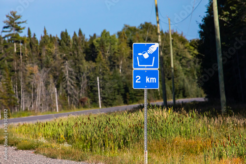 Trash symbol on a blue road sign after 2 km, pine trees forest on the roadsides, Canadian rural roads during a sunny day photo