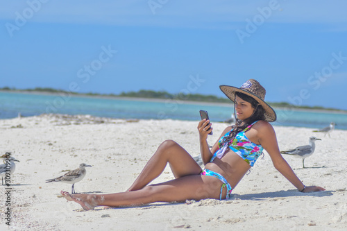 Young african american ethnicity woman using mobile phone to connect social media app on caribbean beach