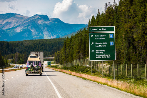Information Road Green Sign, lake Louise, moraine lake, bow valley parkway, Vehicles on Canadian road between forest trees, mountains, Alberta, Canada photo