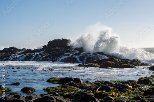 Crashing waves over jagged rocky ocean coastline .