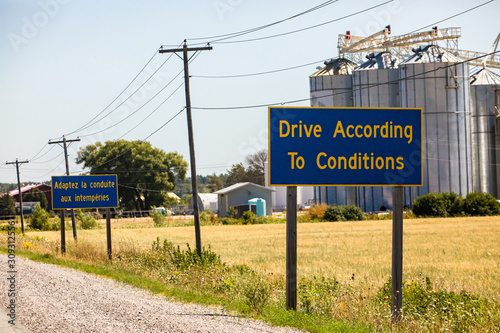 French, English Information road Signs, Drive According To Conditions. Canadian rural country roadside, grain silos in the background, Ontario Canada photo