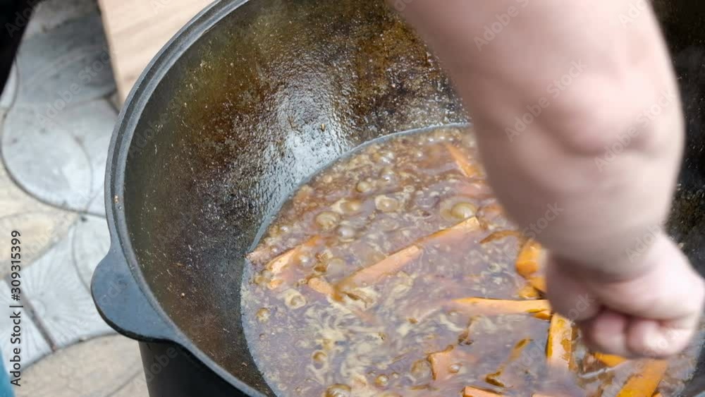 Cooking hot food in a cauldron. A chef's hand stirs a metal spoon with meat and carrots. Close-up. National cuisine of the east. Cooking hot food in a cauldron. A chef's hand stirs a metal spoon with meat and carrots. Close-up. National cuisine of the east.