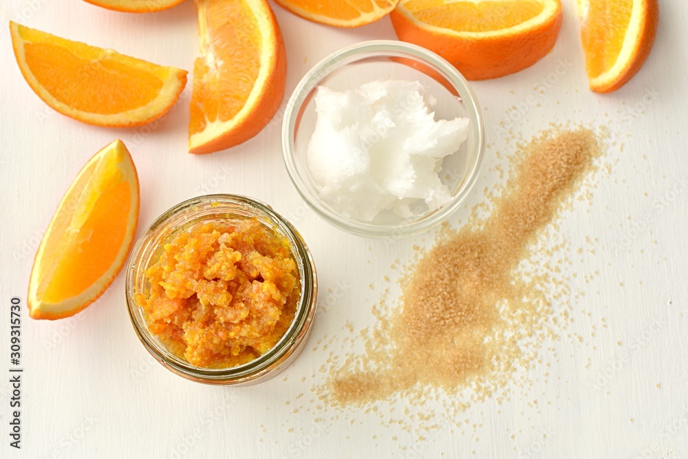 Natural orange body or lip scrub with coconut oil and brown sugar, flat lay on white background. Homemade cosmetics. Natural orange body or lip scrub with coconut oil and brown sugar, flat lay on white background. Homemade cosmetics.