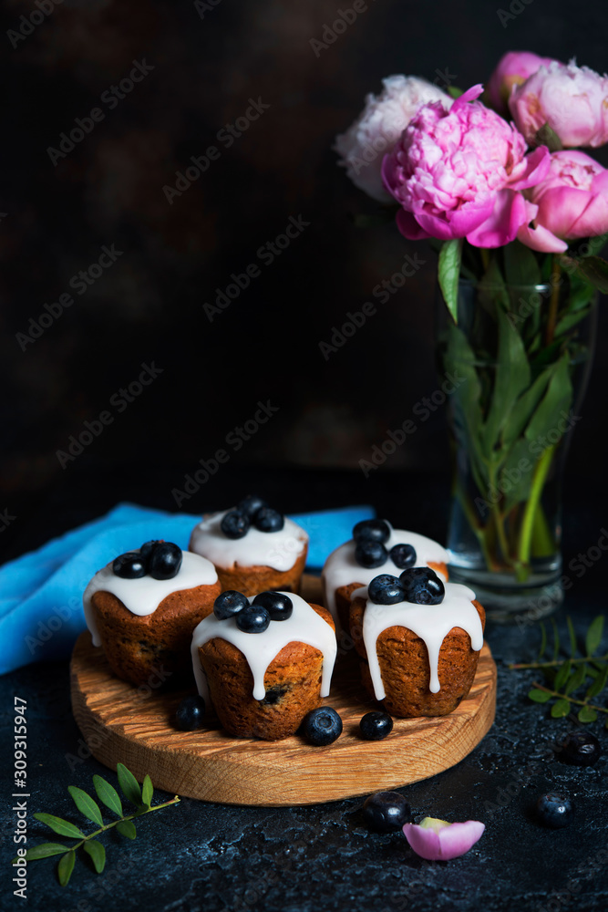 Delicious homemade muffins poured with sugar Fudge and decorated with blueberries on a dark background.