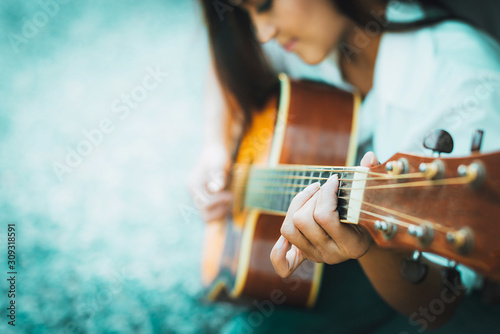 Close up hands of woman playing acoustic guitar with shallow focus on a blurry dark background, Asian female guitarist enjoying learning classic practice music instrument concept