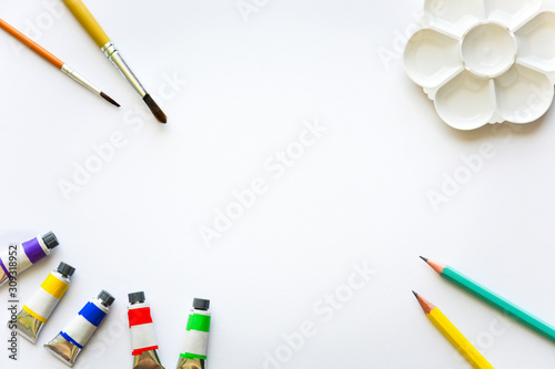 top view of brushes, color tubes, pencils and palette on white drawing pad background, copy space, flat lay, paintings art concept