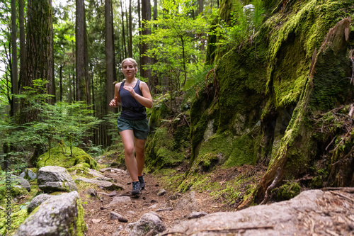 Adventurous Girl Trail Running in the Woods during a vibrant summer day. Taken in Deep Cove  North Vancouver  British Columbia  Canada.