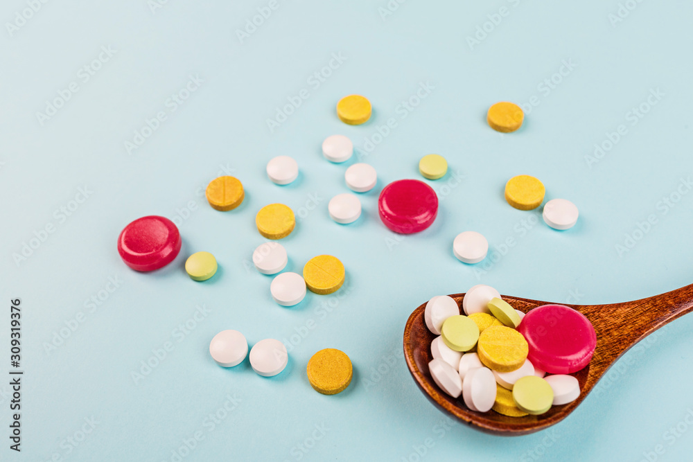 Colorful pills in wooden spoon on a pastel blue background. Flat lay, top view, overhead, mockup, template. Pharmacy and medical concept