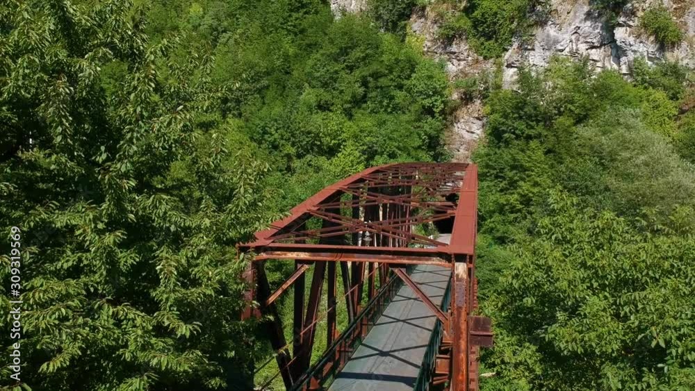 Old railway bridge leading to the mountain cliffs surrounded by trees and other vegetation. Aerial drone descending shot Old railway bridge leading to the mountain cliffs surrounded by trees and other vegetation. Aerial drone descending shot