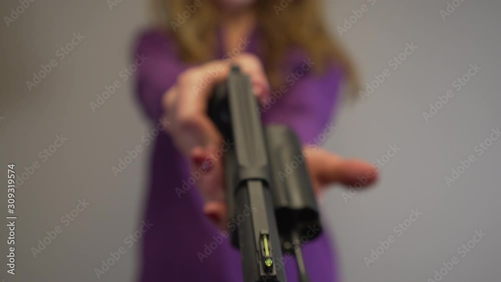 View looking down the barrel of a large black handgun pointed by woman
